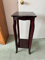 Full view of dark wood plant stand showcasing height, curved legs, and lower shelf.