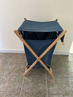 Front angle view of fabric and wood folding laundry hamper on tiled floor