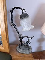 Full view of the lamp showing the flower-shaped glass shade and vine-like arm extending from the base with fairy on swing.