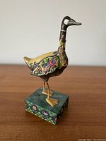 Front angled view of the Jim Shore goose figurine on a patterned square base showing detailed floral designs.