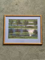 Full view of framed landscape artwork showing trees, water, reflections, and gold frame
