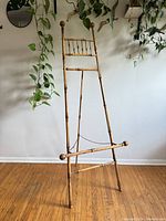 Full view of the large bamboo easel against a wall with plants in the background.