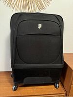 Front view of large black Heys suitcase showing fabric body, front pocket, logo, and spinner wheels.