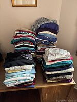 Photo showing multiple stacks of folded tops in various colors and patterns on a table.