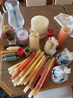 Top down view of assorted candles in various sizes, shapes and colors, including taper candles, votives, pillar candles, and candles wrapped in fabric or ribbon, along with a glass hurricane holder and a napkin.