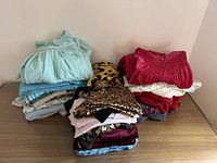 Image showing three stacked piles of folded pajamas and night gowns on a wooden surface, including a light green nightgown, leopard print item, bright red nightgown, and various other pieces.
