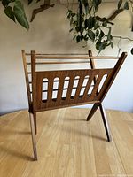 Front-left angled view of the wooden folding magazine rack showing slatted panels and folded leg structure.