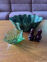Overview photo of entire lot showing large green ceramic leaf-shaped bowl, small green glass bowl with irregular edges, and pair of dark red carved salt and pepper shakers arranged on a wooden table.