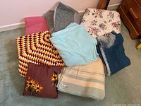 Overview of vintage blankets and cushions arranged on floor showing color, texture, and pattern variety.
