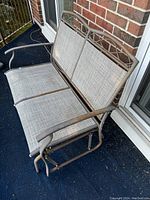 Outdoor metal frame rocking bench with two seating spaces, showing rust on frame and fabric upholstery removed.