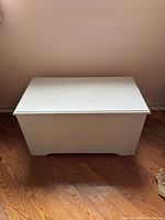 Closed white painted wooden trunk on hardwood floor against a beige wall.