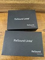 Two black ReSound Unite branded boxes displayed closed on wooden surface
