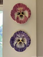 Two pansy flower-shaped ceramic plates mounted on a wall, one pink-purple and one purple-white.
