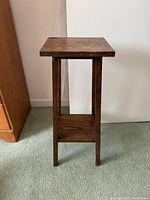 Front view of small wooden plant stand showing rectangular top, four legs and bottom shelf.
