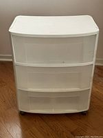 Front view of white plastic three drawer storage tote shelf on caster wheels showing minor wear.
