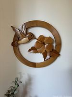 Full view of handcrafted wooden hummingbird inside circular frame hanging on wall.