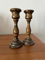 Front view of two wooden candlestick holders showing turned wood and metal-accented bases on wooden surface.
