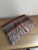 Folded wool blanket with visible red and green stripes on a brownish-beige background on wooden surface.