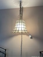 Full view of the ceiling lamp hanging on the ceiling, showing bell-shaped capiz shell shade with metal framing and chain.