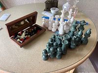 Photo of green and white stone chess pieces arranged on a table next to a wooden box containing magnetic checkers and some chess pieces.