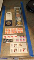 Lot overview showing coins, New Zealand dollar coin, and USPS stamps spread on table.