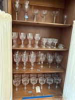 Full set of 64 crystal stemware pieces displayed on wooden shelves, showing a variety of shapes and sizes.