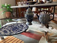 Full view of the three items on a glass table: blue and white plate, teapot, and spherical vase