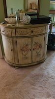 Front view of the demi lune cabinet showing curved shape and floral hand-painted decorations on drawers and cabinet doors.