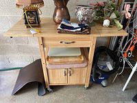 Front view showing drop leaf cabinet with drawer, cutting boards in slot underneath, and wheels.