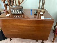 Photo of the wooden drop leaf table from side showing closed leaf and legs with casters, also shows items on table surface and condition.