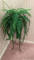 Artificial fern plant in woven basket displayed on the black metal plant stand from a front angle.