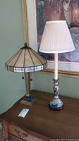 Two table lamps on wood table, one stained glass style and one floral painted with shade
