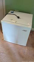 Front view of Arctic King mini fridge on carpet, showing white exterior and power cord on top.