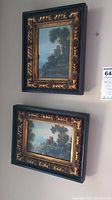 View of both framed paintings hanging on a wall, showing their black and gold carved frames and landscape scenes.