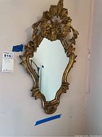 Full view of the ornately framed mirror hanging on a wall with a curved and carved gold design.