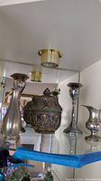Photo showing two pewter candlesticks flanking a decorative covered jar with detailed metalwork.