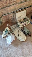 Photo showing the sewing box with its lid open displaying various sewing notions, along with the mini ironing board and two irons placed on the floor.