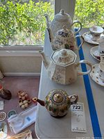 Four decorative teapots arranged on a table by window natural light. Various styles and designs visible.
