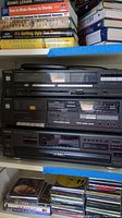 Front view of stacked Technics stereo equipment showing the 5-disc CD changer on top, stereo cassette deck in middle, and AM/FM receiver at bottom, all black finish with multiple buttons and digital displays.