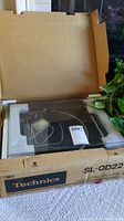 Technics SL-QD22 turntable in original packaging with visible clear dust cover and foam protection inside a worn cardboard box.