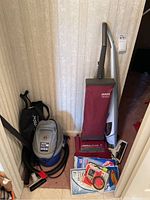 Two vacuum cleaners side by side. One upright Hoover Elite 400 with red bag and one silver-blue King's Up canister vacuum with hose and powerhead attachment.