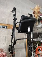 Side view of the black rolling walker showing the seat, backrest, and wheels.