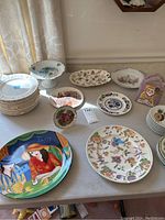 Wide image showing the group of assorted china pieces including plates, bowls, and decorative items arranged on a table.