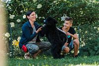Trainer kneeling in backyard interacting with black dog and owner’s child