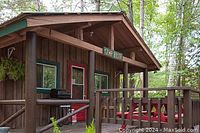 Exterior front view of wooden cottage with covered deck, railing and seating