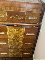 Close-up photo of the upper and middle drawers showing decorative inlays and wood texture with brass accent