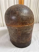 Front and side view of antique hardwood hat shaping mold showing natural wood grain and patina, circular groove near midpoint, and surface cracks.