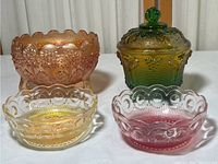 Four carnival glass pieces including amber three-legged bowl, red-yellow bowl, small clear-yellow bowl, and green covered dish