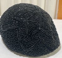 Front side view of a black fabric hat heavily decorated with small black beads and sequins in floral and geometric patterns.