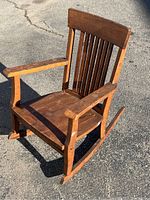 Front angle view of the vintage handmade hardwood children's rocking chair, showing spine slatted backrest, armrests, and rockers.